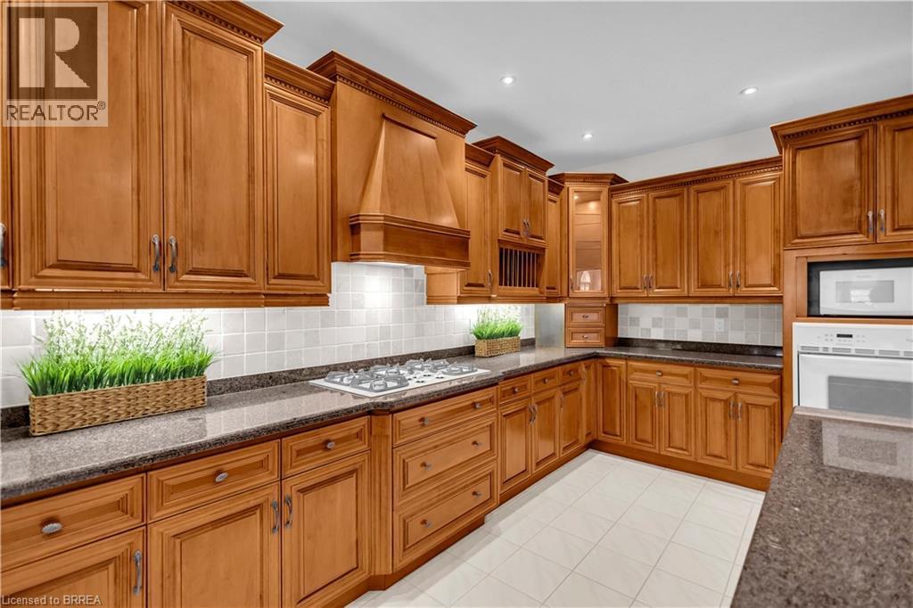Kitchen featuring extensive wood cabinetry, dark speckled countertops, a tile backsplash, a built-in microwave, and a gas cooktop - 302 German School Road, Paris, ON