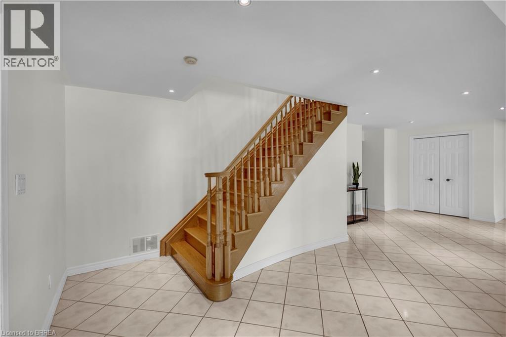 Wood-finish staircase with baluster railing, recessed lighting, diagonal tile flooring, and white bifold closet doors - 302 German School Road, Paris, ON