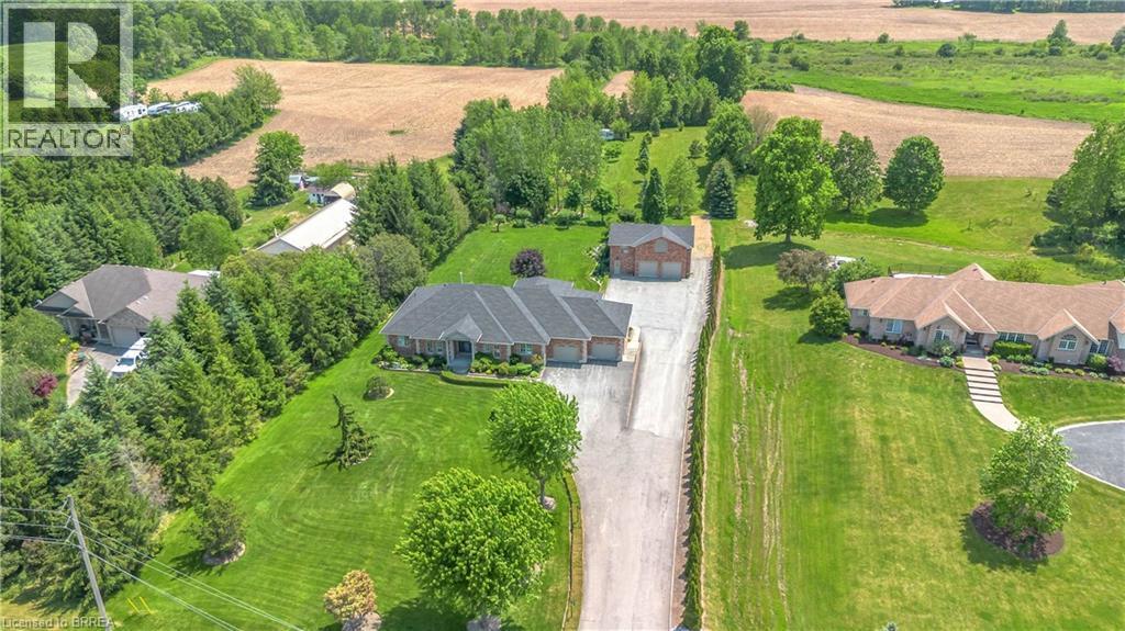 Expansive property featuring a brick residence with a gabled roofline, a lengthy paved driveway, mature trees, and an additional brick outbuilding - 302 German School Road, Paris, ON