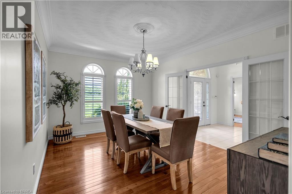 Dining area featuring wood-finish flooring, three arched windows with plantation shutters, crown molding, and a decorative ceiling medallion with a chandelier - 302 German School Road, Paris, ON