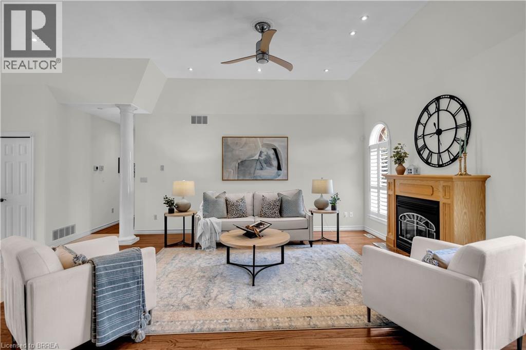 Spacious living area featuring vaulted ceilings, recessed lighting, wood-finish flooring, a wood mantle fireplace, and a decorative column - 302 German School Road, Paris, ON