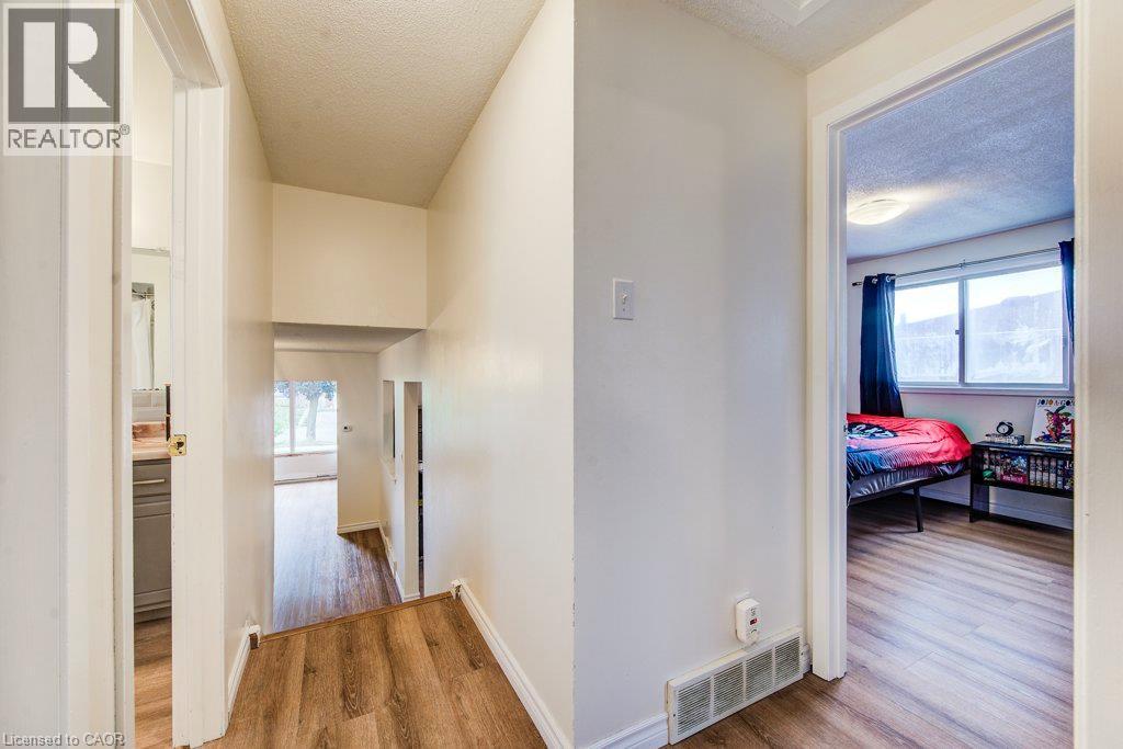 Wood-finish flooring throughout, white painted walls, and an open doorway to a room featuring a window and overhead light fixture - 143 Sunrise Place, Kitchener, ON