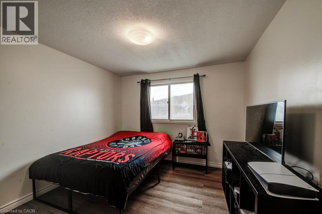 Bright secondary bedroom featuring wood-finish flooring, recessed ceiling lighting, and a large window with blackout curtains - 143 Sunrise Place, Kitchener, ON