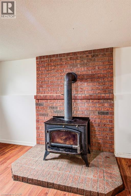 Wood-burning stove set against a brick accent wall, featuring a tiled hearth and wood-finish flooring - 143 Sunrise Place, Kitchener, ON