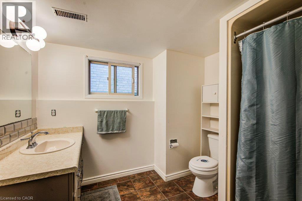 Bathroom featuring a single vanity with an integrated sink, a sliding window, built-in shelving, and a shower with a curtain rod - 143 Sunrise Place, Kitchener, ON