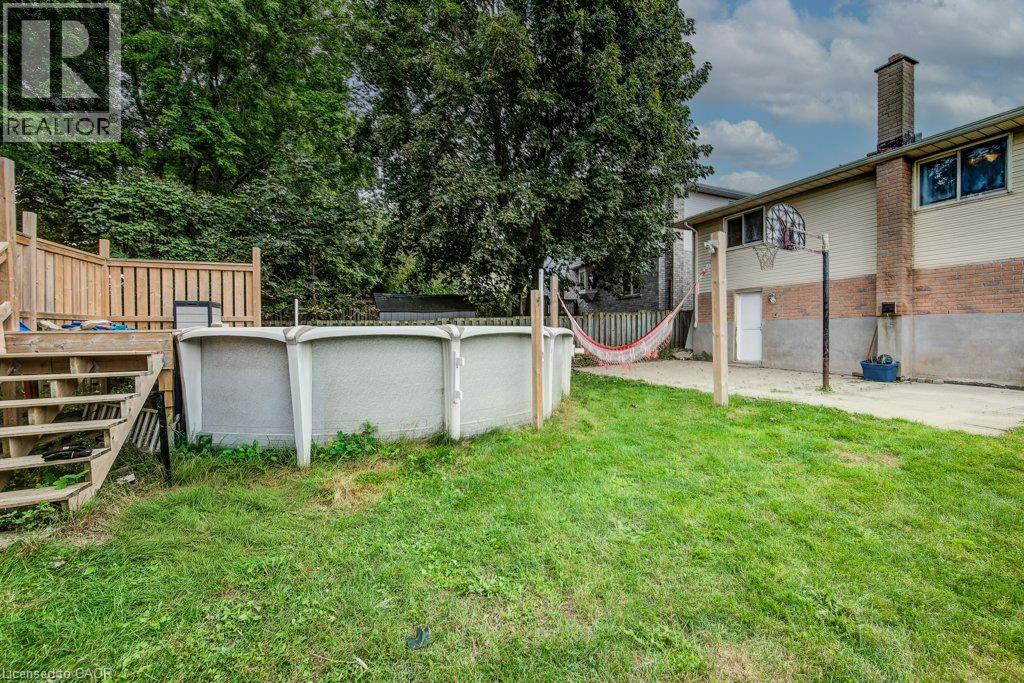Expansive backyard featuring a wood deck with stairs and railing, an above-ground pool, a concrete patio area, and a basketball hoop - 143 Sunrise Place, Kitchener, ON
