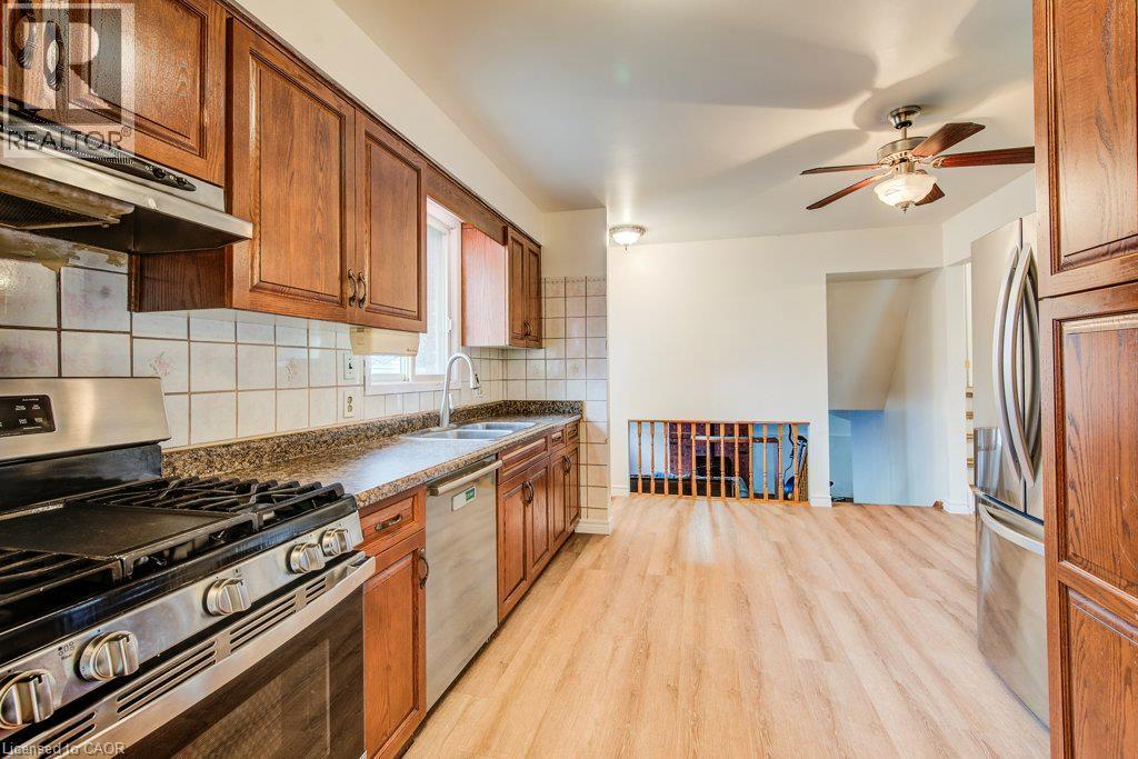 Wood-finish flooring, stainless steel appliances, wood cabinetry, tile backsplash, and a ceiling fan - 143 Sunrise Place, Kitchener, ON