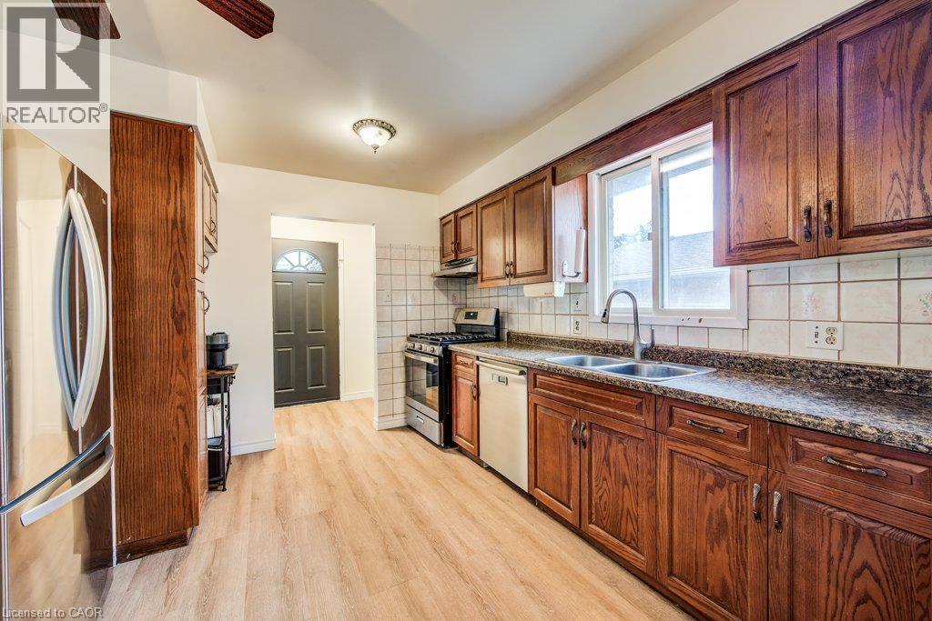 Galley kitchen showcasing wood-finish cabinetry with hardware accents, stainless steel appliances including a refrigerator and range, granite-style countertops, subway tile backsplash, and wood-finish - 143 Sunrise Place, Kitchener, ON