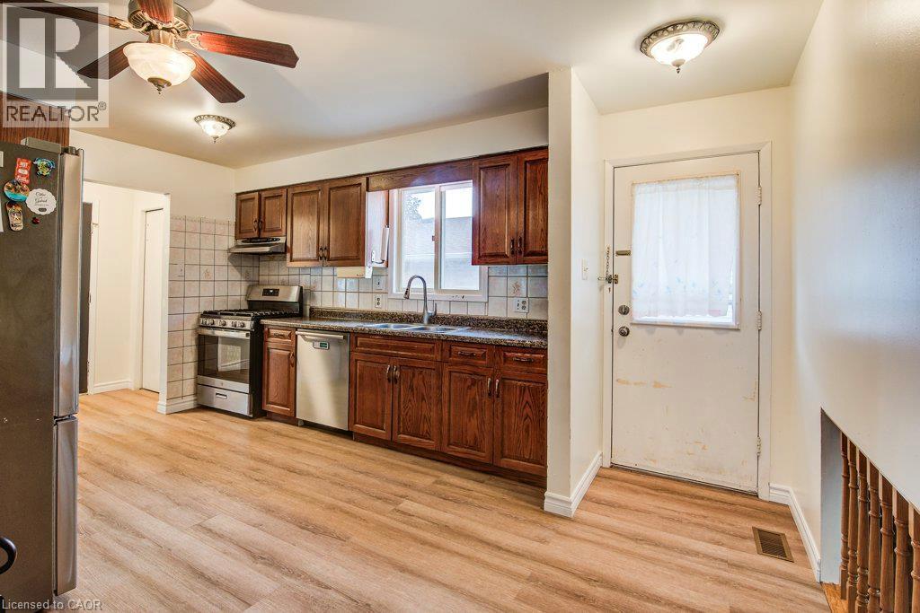 Kitchen with wood-finish flooring, dark wood cabinetry, a tile backsplash, and stainless steel appliances - 143 Sunrise Place, Kitchener, ON