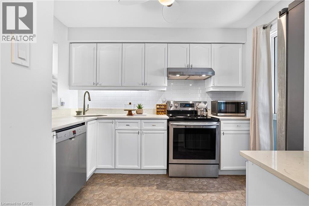 White cabinetry with brushed nickel hardware, stainless steel appliances, light-toned countertops, white subway tile backsplash, and hexagonal floor tiling - 1517 Elm Road Unit# 9, Oakville, ON