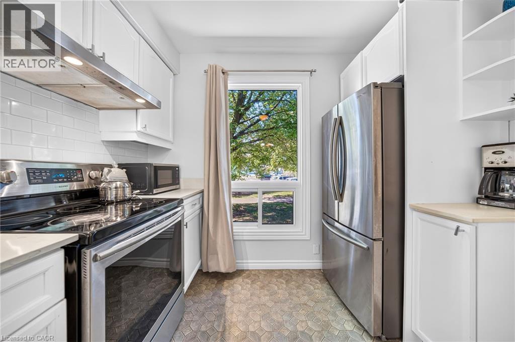 Kitchen featuring white cabinetry, stainless steel appliances, subway tile backsplash, and patterned floor tiling - 1517 Elm Road Unit# 9, Oakville, ON