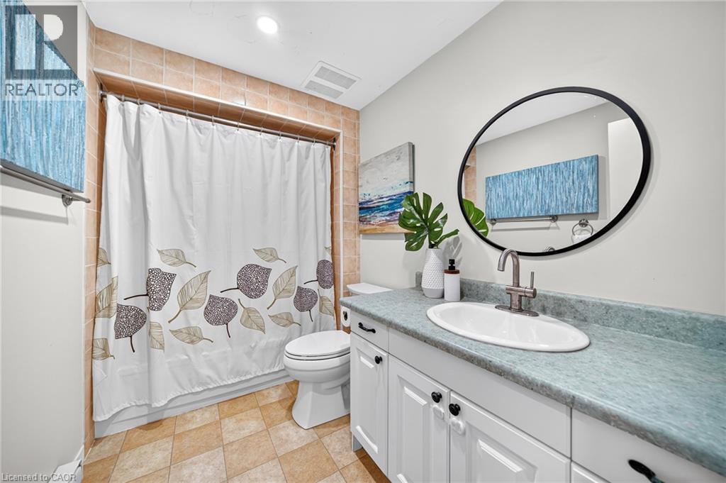 White vanity with black cabinet hardware, oval undermount sink, and a circular black-framed mirror - 1517 Elm Road Unit# 9, Oakville, ON