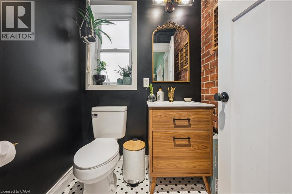 Bathroom featuring a wood-finish vanity with drawer storage, a white ceramic sink, a patterned tile floor, and an exposed brick accent wall - 58 Balmoral Avenue N, Hamilton, ON
