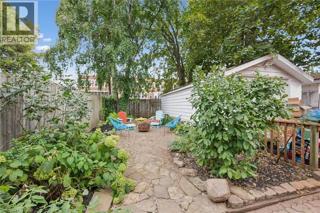 Mature backyard featuring established shade trees, garden beds with lush plantings, stone pathway and pea gravel patio - 58 Balmoral Avenue N, Hamilton, ON
