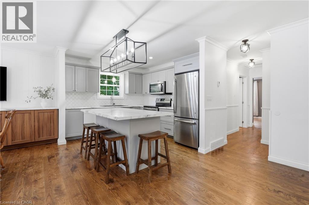 Modern kitchen featuring a central island with countertop seating, light-toned cabinetry, stainless steel appliances, and a tiled backsplash - 72 Crestlynn Crescent, Simcoe, ON