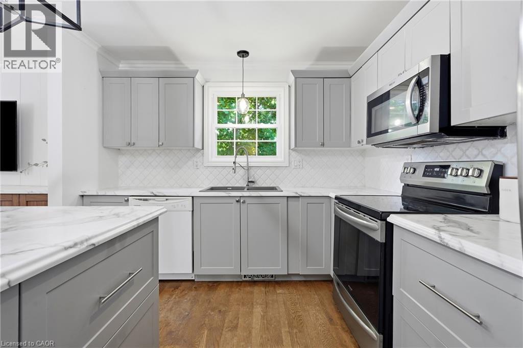 Kitchen featuring light gray and white cabinetry, stone-finish countertops, stainless steel appliances, a white diamond-patterned backsplash, and wood-finish flooring - 72 Crestlynn Crescent, Simcoe, ON