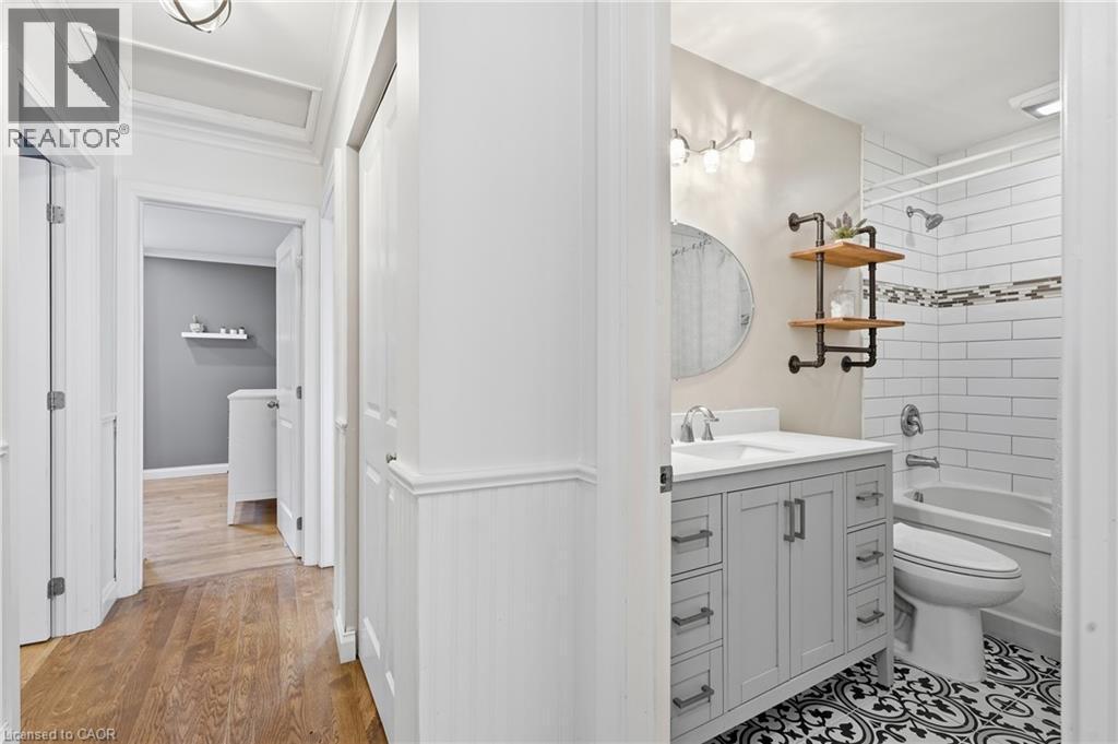 Bathroom featuring a single vanity with a solid surface countertop, white subway tile shower surround with an accent band, patterned floor tile, and a built-in tub - 72 Crestlynn Crescent, Simcoe, ON