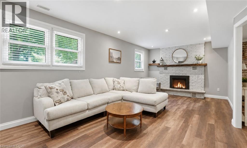 Inviting living area featuring a whitewashed brick fireplace with a wood mantel, wood-finish flooring, recessed lighting, and multiple windows - 72 Crestlynn Crescent, Simcoe, ON