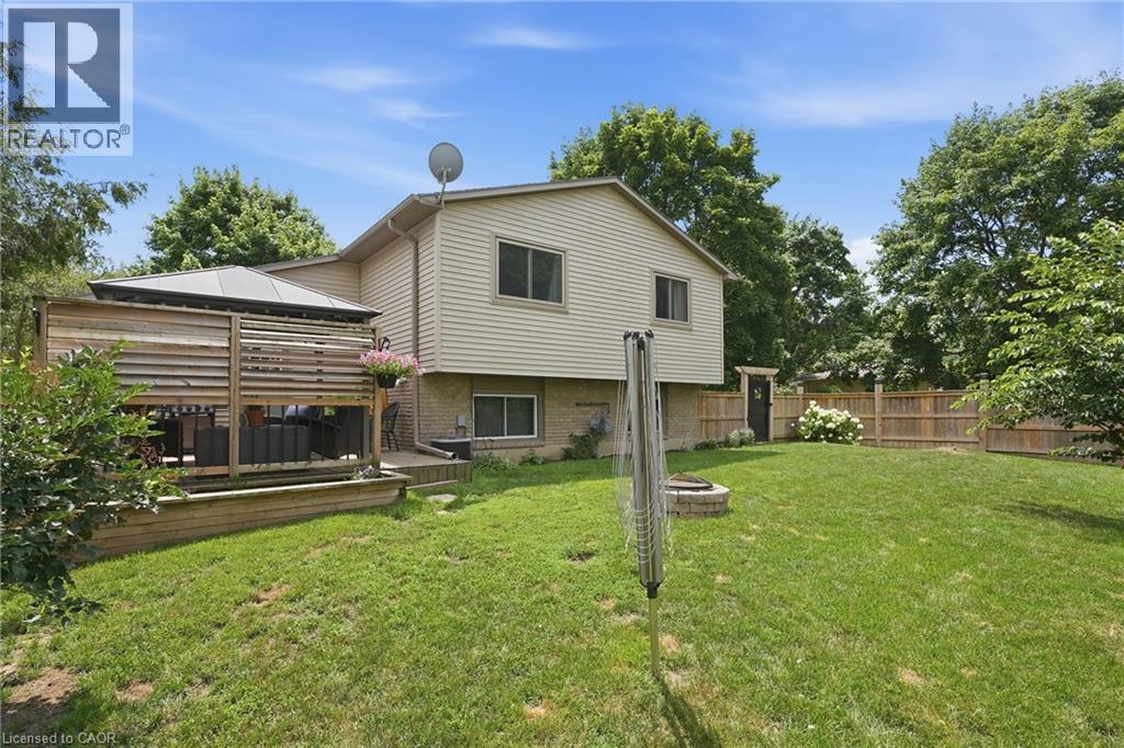 Expansive backyard featuring a covered patio with slatted wood detailing, a built-in fire pit, a perimeter wood fence, and mature trees - 72 Crestlynn Crescent, Simcoe, ON
