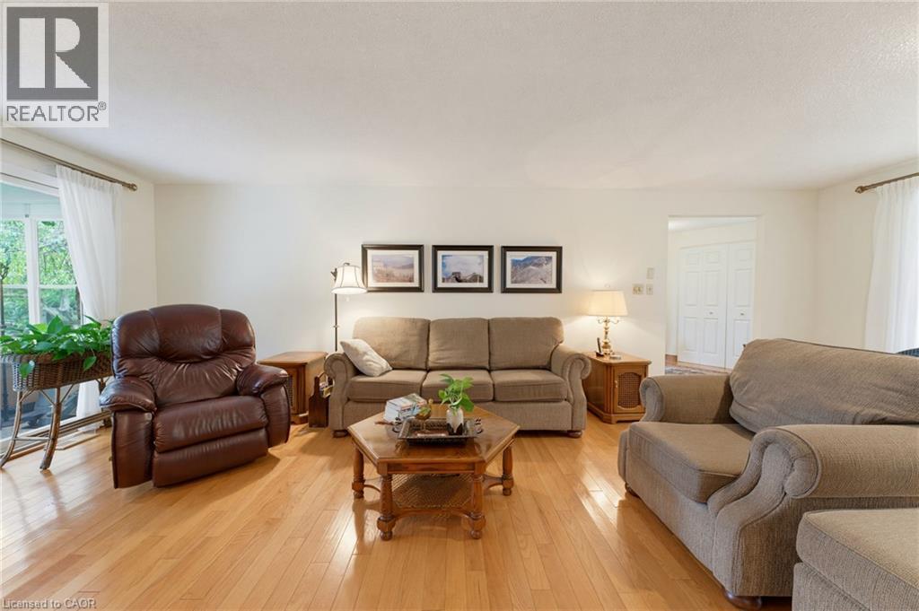 Spacious living room with warm wood-finish flooring, multiple seating areas, and abundant natural light from dual windows - 15 Mclaren Avenue N, Listowel, ON