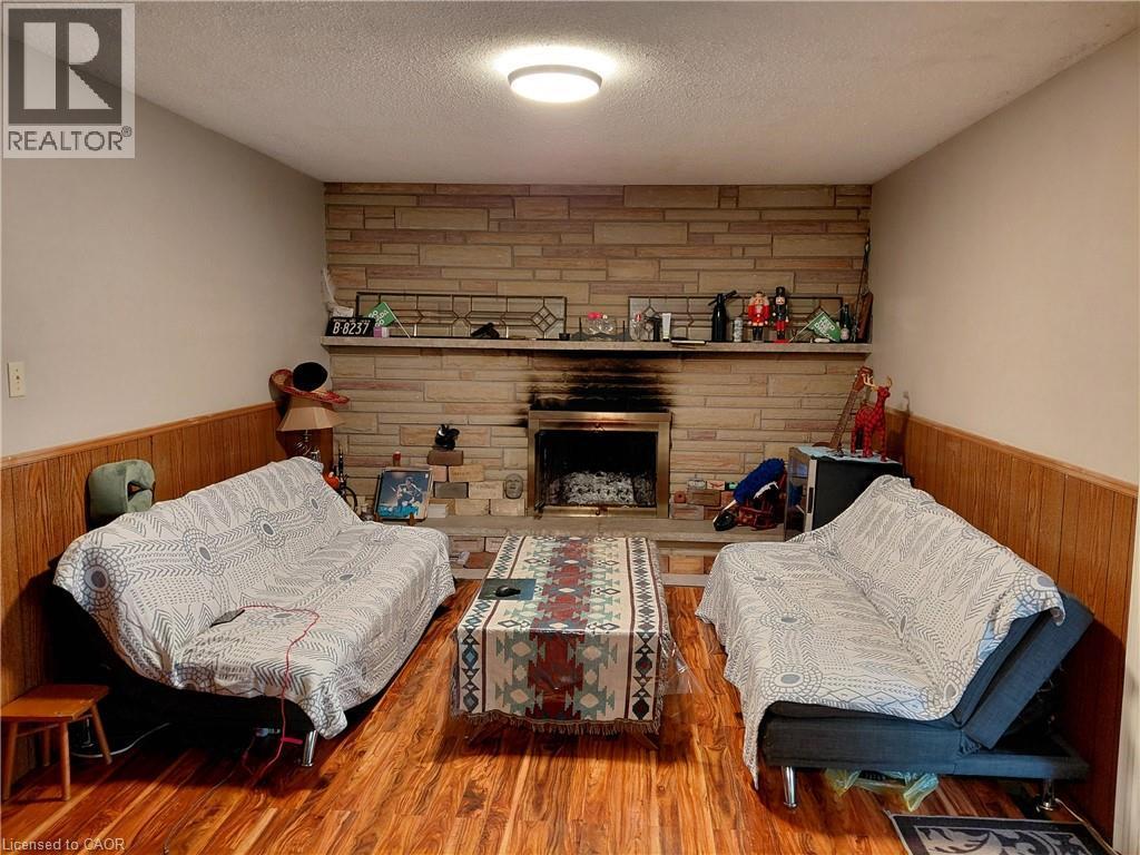 Wood-finish flooring, stone-clad fireplace with hearth, and wood paneling - 244 Guildwood Drive, Hamilton, ON