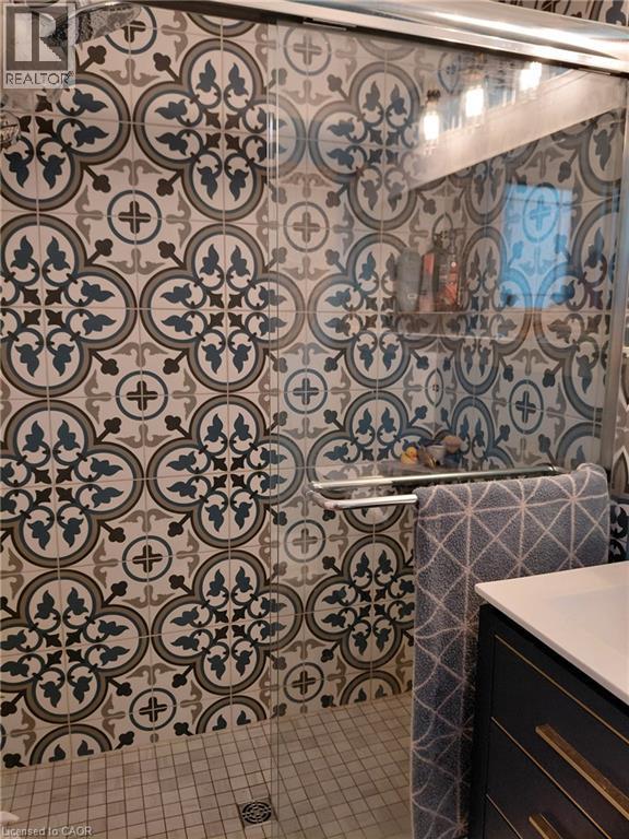 Patterned wall tile in a shower enclosure with a glass door, integrated shower niche, and mosaic tile floor - 244 Guildwood Drive, Hamilton, ON