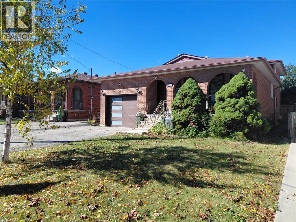 Brick exterior with arched window openings, a contemporary garage door, and a front yard with established plantings - 244 Guildwood Drive, Hamilton, ON