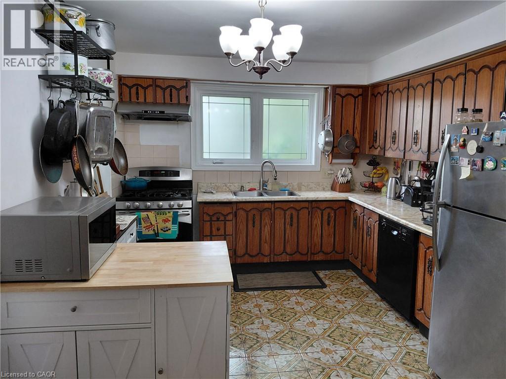 U-shaped kitchen with wood-finish cabinetry, stainless steel refrigerator, and patterned floor tile - 244 Guildwood Drive, Hamilton, ON