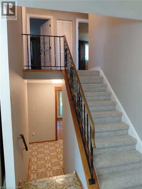 Carpeted staircase with an ornate wrought iron and wood handrail, leading to an upper landing with a matching wrought iron railing - 244 Guildwood Drive, Hamilton, ON