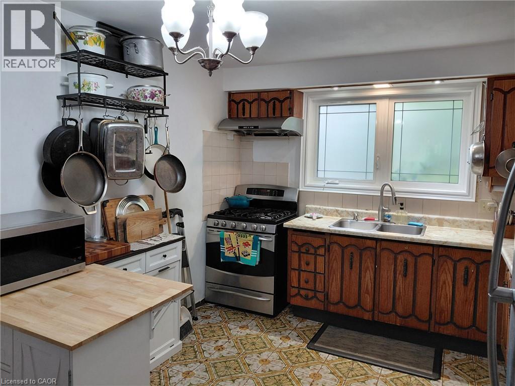 Kitchen featuring wood-finish cabinetry, a double basin stainless steel sink, a gas range with a range hood, and patterned floor tiling - 244 Guildwood Drive, Hamilton, ON