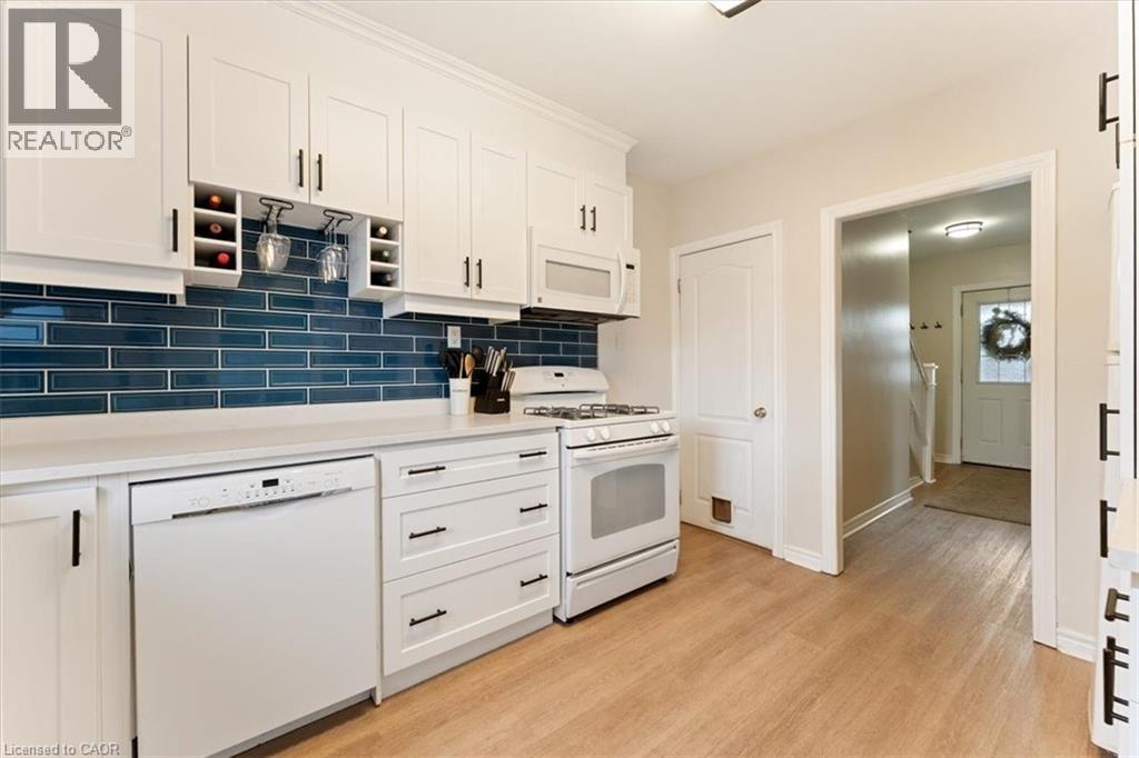 Kitchen featuring white cabinetry, a blue subway tile backsplash, light countertops, and wood-finish flooring - 17 Craigmiller Avenue, Hamilton, ON
