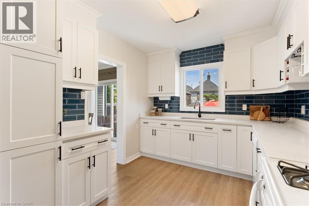 Kitchen featuring white shaker-style cabinetry with matte black hardware, light-toned countertops, a deep blue subway tile backsplash, and wood-finish flooring - 17 Craigmiller Avenue, Hamilton, ON