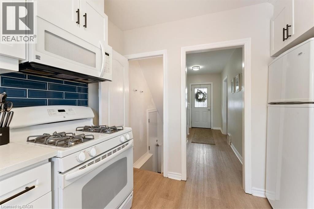 Kitchen featuring white cabinetry with dark hardware, a white range with an above-range microwave, white refrigerator, and a blue subway tile backsplash - 17 Craigmiller Avenue, Hamilton, ON