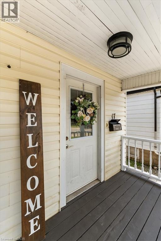Covered front porch featuring wood-finish flooring, light-colored siding, and a white entry door with a glass pane - 17 Craigmiller Avenue, Hamilton, ON