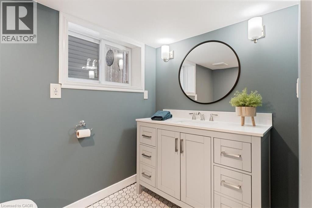 Bathroom featuring a white vanity with brushed nickel hardware, white countertop, and a circular black-framed mirror - 17 Craigmiller Avenue, Hamilton, ON
