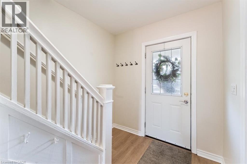 Entryway featuring a white paneled door with decorative glass, wood-finish flooring, and a staircase with white balusters and newel post - 17 Craigmiller Avenue, Hamilton, ON