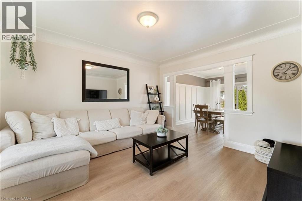 Living area featuring crown molding, light wood-finish flooring, and a cased opening to a dining area with board and batten wall treatment - 17 Craigmiller Avenue, Hamilton, ON