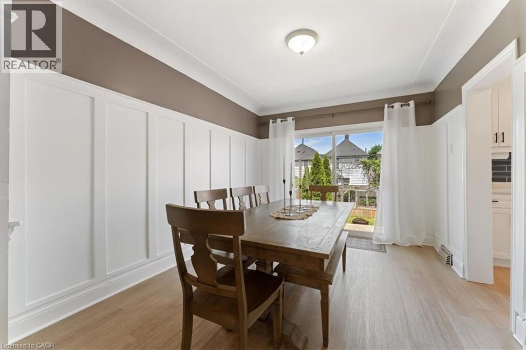Dining area featuring light wood-finish flooring, white board and batten paneling, a neutral-toned upper wall, and a ceiling-mounted light fixture - 17 Craigmiller Avenue, Hamilton, ON