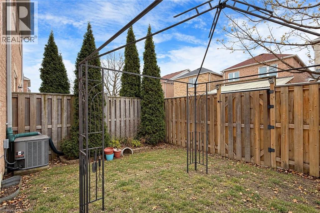 Enclosed backyard with a wood privacy fence, featuring a metal arbor and established evergreen trees - 21 Eastview Gate Unit# 36, Brampton, ON