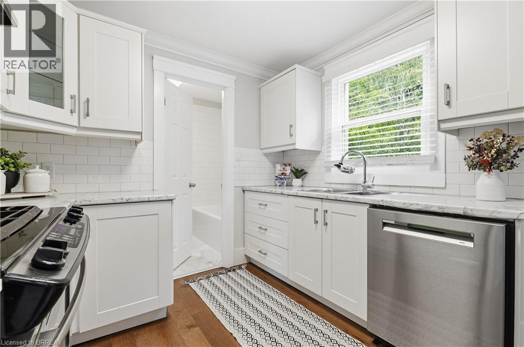 White shaker-style cabinetry, subway tile backsplash, stainless steel appliances, light-toned countertops, and wood-finish flooring - 87 Strathcona Avenue, Brantford, ON