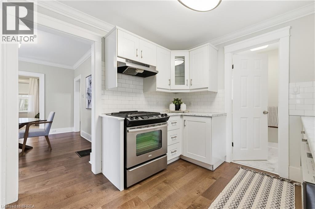 Stainless steel range with overhead ventilation, white shaker-style cabinetry, white subway tile backsplash, light-colored countertops, and wood-finish flooring - 87 Strathcona Avenue, Brantford, ON