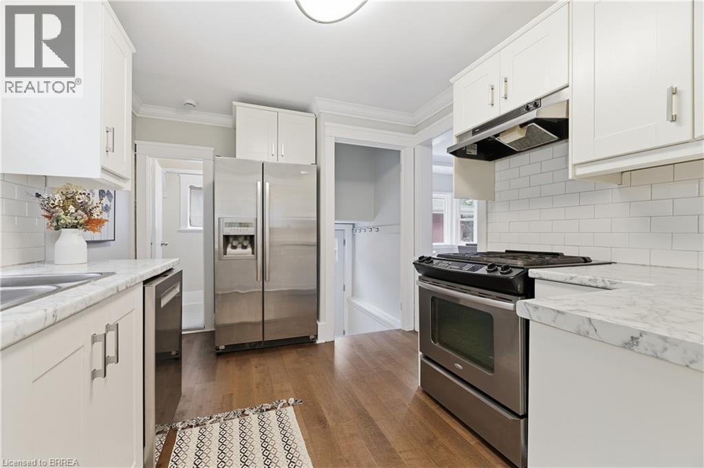 White cabinetry, stainless steel appliances, wood-finish flooring, subway tile backsplash, and stone-finish countertops - 87 Strathcona Avenue, Brantford, ON