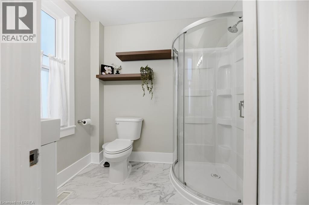 Curved glass shower enclosure, white shower surround, floating wood shelves, white toilet, and patterned floor tile - 87 Strathcona Avenue, Brantford, ON