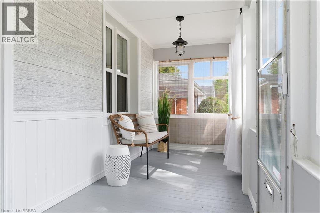 Enclosed porch with wide plank flooring, beadboard wainscoting, and a hanging light fixture - 87 Strathcona Avenue, Brantford, ON