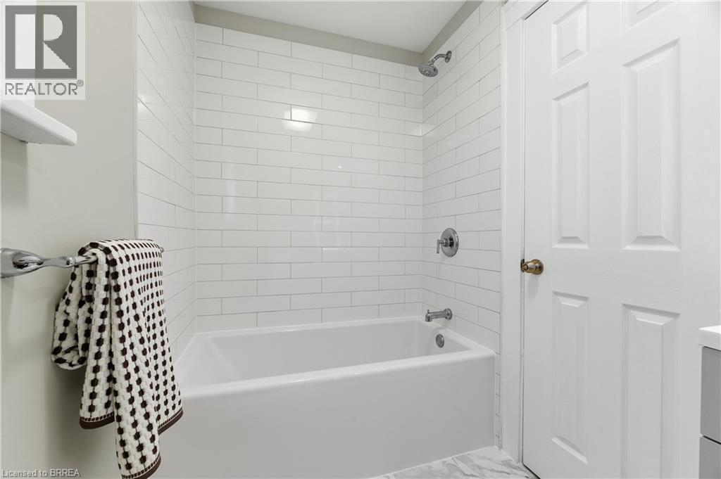 White subway tile shower surround, chrome shower and tub fixtures, white paneled door, and marble-look flooring - 87 Strathcona Avenue, Brantford, ON