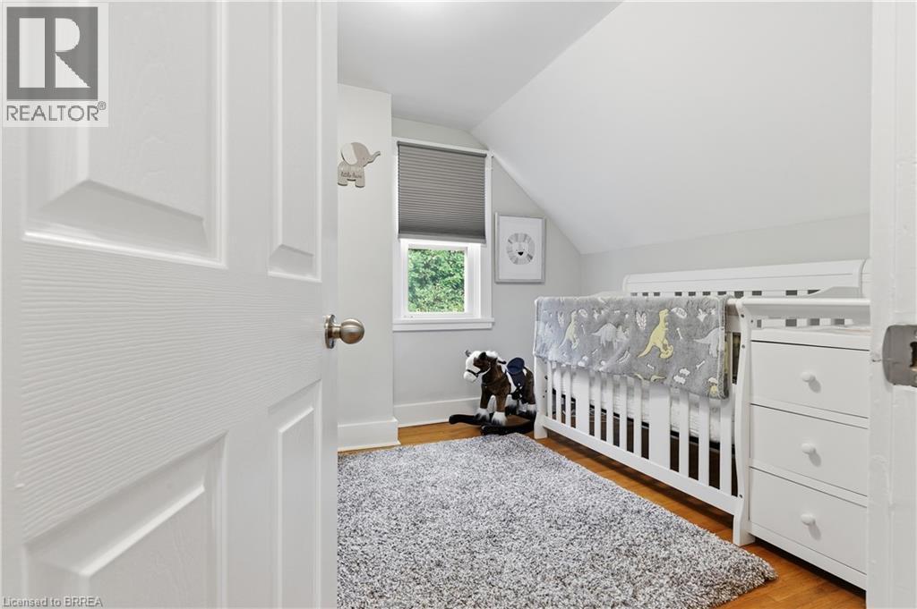 Wood-finish flooring with a white trim, a built-in window with a neutral shade, and a white paneled door - 87 Strathcona Avenue, Brantford, ON