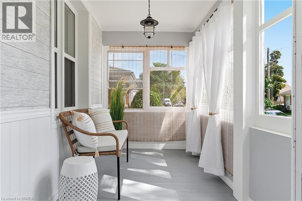 Enclosed porch featuring shiplap accent walls, wood-finish flooring, multiple windows, and a hanging light fixture - 87 Strathcona Avenue, Brantford, ON