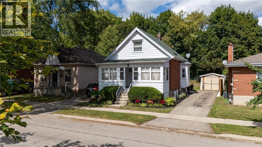 White siding exterior with brick accents, prominent front porch, mature landscaping, paved driveway, and detached garage - 87 Strathcona Avenue, Brantford, ON