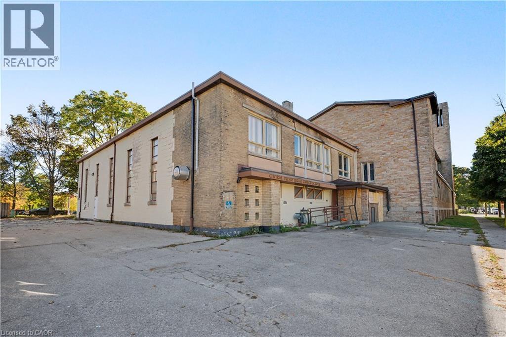 Brick exterior with multiple window configurations and a concrete parking area - 97 Wellington Street, Brantford, ON