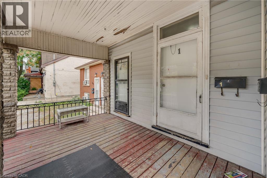 Covered front porch featuring wood-finish flooring, stone-clad columns, and wrought iron railing - 211 Wentworth Street N, Hamilton, ON